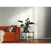 Papier peint intissé clair avec motif de feuilles graphique dans un salon moderne avec canapé orange, table d'appoint et plante d'intérieur.