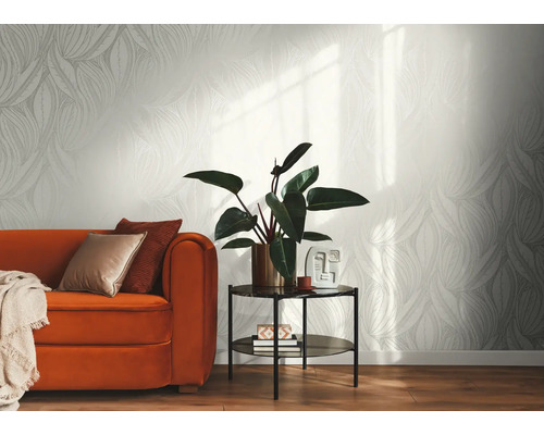 Papier peint intissé clair avec motif de feuilles graphique dans un salon moderne avec canapé orange, table d'appoint et plante d'intérieur.