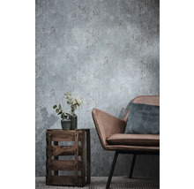 Papier peint intissé aspect béton dans un salon avec un fauteuil en similicuir et une caisse en bois servant de table d'appoint.
