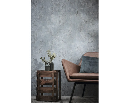 Papier peint intissé aspect béton dans un salon avec un fauteuil en similicuir et une caisse en bois servant de table d'appoint.
