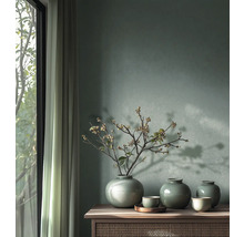 Mur peint en vert avec trois vases en céramique à glaçure craquelée et des branches sur un buffet en bois à côté d'une fenêtre lumineuse.