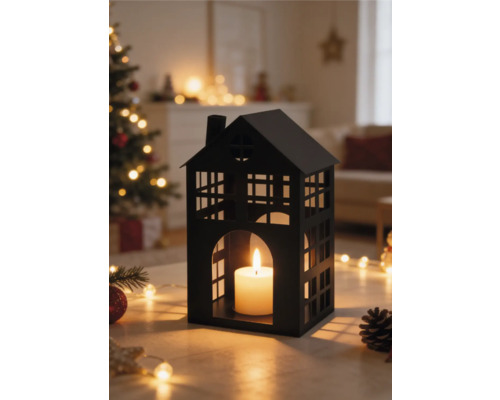 Lanterne noire en métal en forme de maison avec bougie dans un salon lumineux avec sapin de Noël et guirlandes.