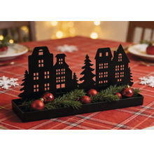Décoration de Noël noire en métal avec silhouette de maisons, branches de sapin et boules rouges dans un plateau sur une table décorée.