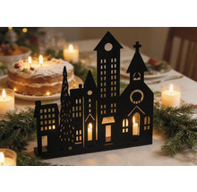 Silhouette noire d'une ville d'hiver servant de bougeoir sur une table de fête avec des branches de sapin et des bougies.