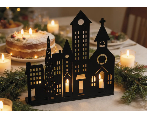 Silhouette noire d'une ville d'hiver servant de bougeoir sur une table de fête avec des branches de sapin et des bougies.
