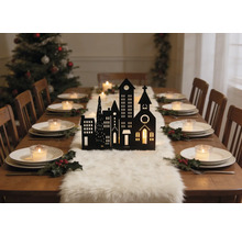Table bois avec silhouette de ville noire, chemin de table en fourrure blanche, bougies et houx. Sapin de Noël à l arrière-plan.