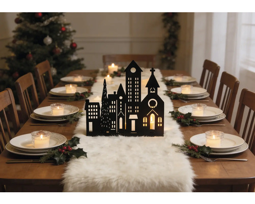 Table bois avec silhouette de ville noire, chemin de table en fourrure blanche, bougies et houx. Sapin de Noël à l arrière-plan.