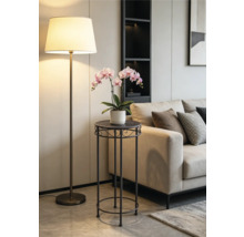 Porte-plante moderne en métal sombre avec une orchidée rose dans un salon lumineux à côté d'un canapé beige et d'un lampadaire.
