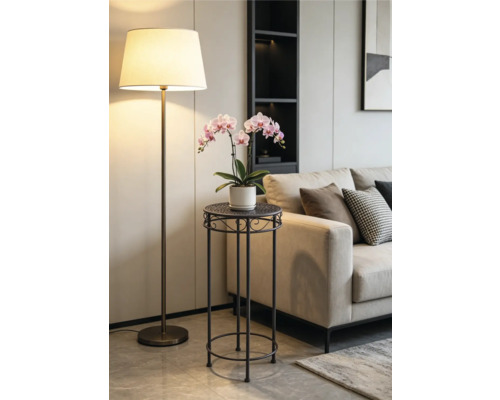 Porte-plante moderne en métal sombre avec une orchidée rose dans un salon lumineux à côté d'un canapé beige et d'un lampadaire.