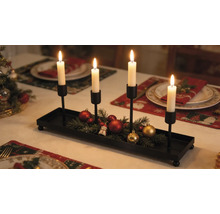 Porte-bougies de l'Avent en métal noir avec quatre bougeoirs, décoré de branches de sapin et de boules de Noël sur une table dressée pour les fêtes.