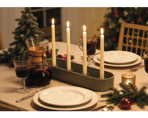Bougeoir de l'Avent avec quatre bougies allumées sur une table de Noël dressée avec de la vaisselle et des décorations.