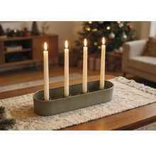 Bougeoir ovale vert avec quatre bougies blanches allumées sur un chemin de table dans un salon décoré pour Noël.