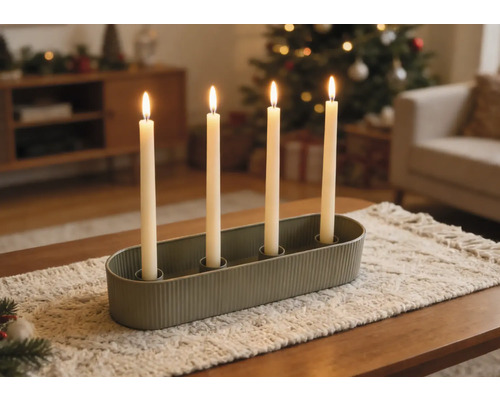 Bougeoir ovale vert avec quatre bougies blanches allumées sur un chemin de table dans un salon décoré pour Noël.