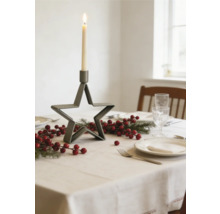 Table de fête dressée avec bougeoir en métal en forme d étoile, branches de sapin et baies rouges sur une nappe claire.