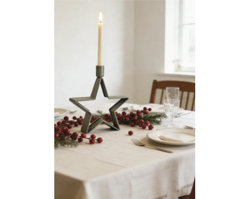 Table de fête dressée avec bougeoir en métal en forme d étoile, branches de sapin et baies rouges sur une nappe claire.