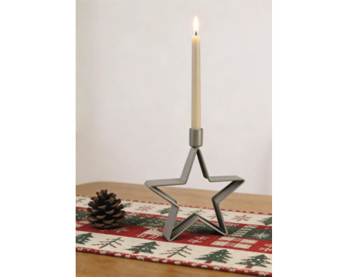 Chandelier en forme d'étoile en métal nervuré avec une bougie allumée, à côté d'une pomme de pin sur un chemin de table festif.