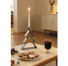 Chandelier nervuré en métal en forme de sapin de Noël avec une bougie blanche allumée sur une table à côté de biscuits et un verre de boisson chaude.