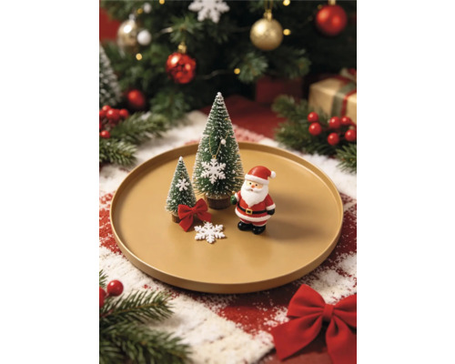 Décoration de Noël sur une assiette avec une figurine de Père Noël, deux sapins miniatures et des flocons de neige sur fond festif lumineux.