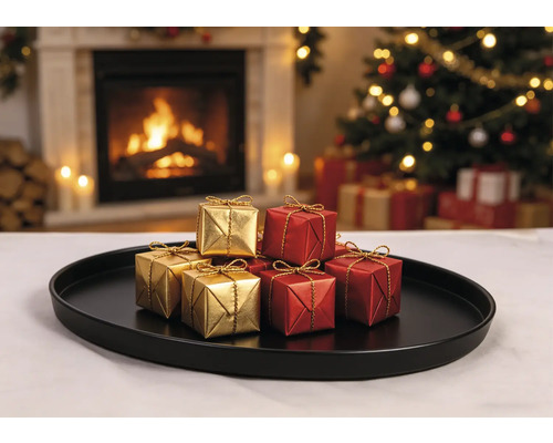 Petites boîtes cadeaux dorées et rouges avec rubans dorés sur un plateau noir devant une cheminée allumée et un sapin de Noël.