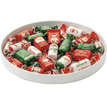 Coupe remplie de bonbons de Noël emballés dans du papier festif avec des motifs de Père Noël, bonhomme de neige et sapin.