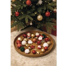 Plateau rond rempli de diverses décorations de Noël comme des boules, des figurines de Père Noël et des étoiles sous un sapin de Noël décoré.