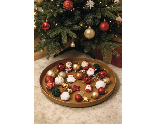 Plateau rond rempli de diverses décorations de Noël comme des boules, des figurines de Père Noël et des étoiles sous un sapin de Noël décoré.