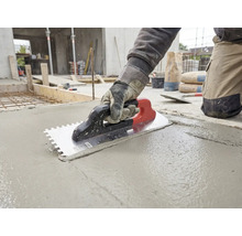Handwerker glättet mit einer Zahnkelle frischen Beton auf einer Baustelle.