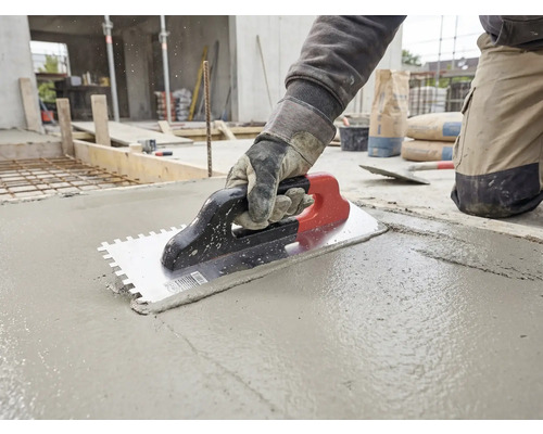 Handwerker glättet mit einer Zahnkelle frischen Beton auf einer Baustelle.