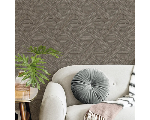 Tapete mit braunem geometrischem Muster hinter einem grauen Sofa mit rundem Samtkissen und einer Zimmerpflanze.