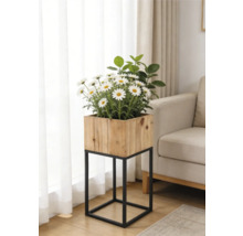 Jardinière carrée en bois sur un support en métal noir avec des marguerites blanches dans un salon lumineux à côté d'un canapé.