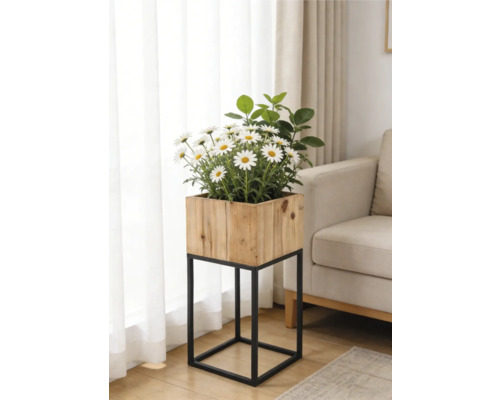 Jardinière carrée en bois sur un support en métal noir avec des marguerites blanches dans un salon lumineux à côté d'un canapé.