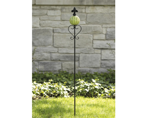 Tuteur de jardin en métal noir avec boule en céramique nervurée verte, volutes décoratives et pointe fleur de lys dans un jardin.
