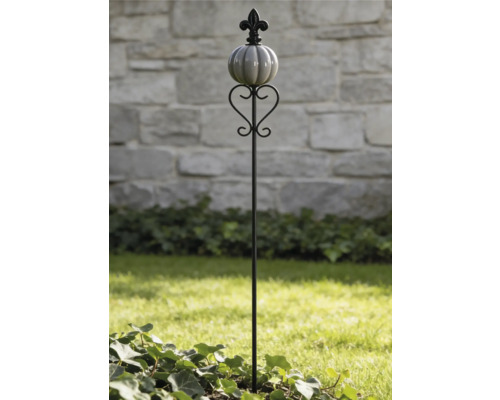 Tuteur de jardin avec fleur de lys, boule nervurée et décoration en forme de cœur dans un jardin lumineux.