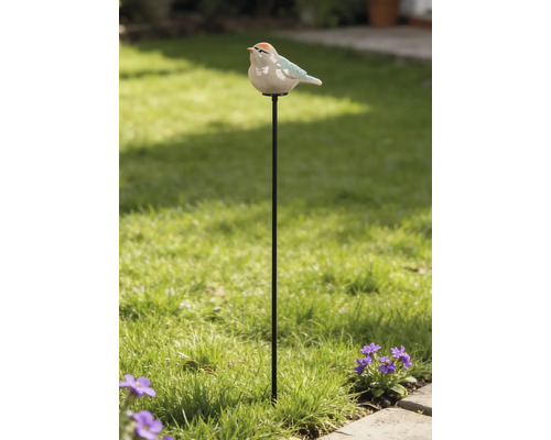 Pic de jardin en métal avec une figurine d'oiseau en céramique dans un jardin lumineux avec pelouse et fleurs.