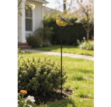 Gartenstecker mit einer Vogelfigur auf einem Metallstab, platziert in einem hellen Gartenbeet neben einem Strauch.
