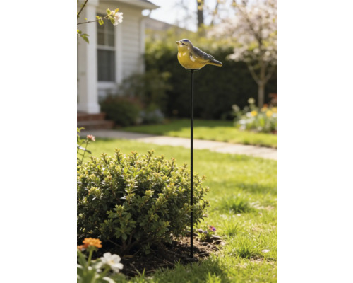 Gartenstecker mit einer Vogelfigur auf einem Metallstab, platziert in einem hellen Gartenbeet neben einem Strauch.