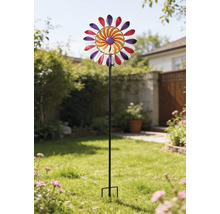 Éolienne multicolore en métal sur une tige noire, placée dans un jardin lumineux sur une pelouse.