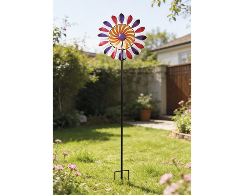 Éolienne multicolore en métal sur une tige noire, placée dans un jardin lumineux sur une pelouse.