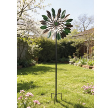 Dekoratives Windspiel aus Metall in Blätterform auf einem schwarzen Stab in einem hellen, gepflegten Garten.