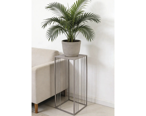 Support à plantes carré en métal gris avec barres verticales, avec une plante verte en pot à côté d'un canapé.
