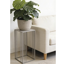 Support pour plantes moderne en métal gris au design minimaliste, avec une plante verte en pot à côté d un canapé clair dans un salon.