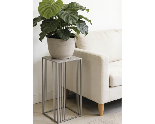 Support pour plantes moderne en métal gris au design minimaliste, avec une plante verte en pot à côté d un canapé clair dans un salon.