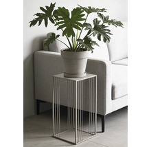 Support pour plantes moderne en métal avec structure filaire carrée, portant une plante en pot, dans un salon à côté d'un canapé.