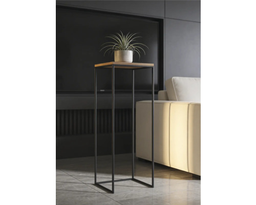 Support de plante moderne et haut avec plateau carré en bois et structure en métal noir dans un salon lumineux à côté d'un canapé.