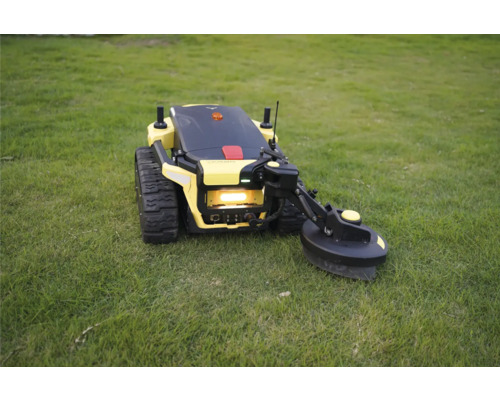 Robot tondeuse jaune avec entraînement par chenilles et bras de coupe latéral sur une pelouse.