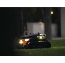 Robot de jardin autonome Yarbo sur une pelouse la nuit avec phares allumés.