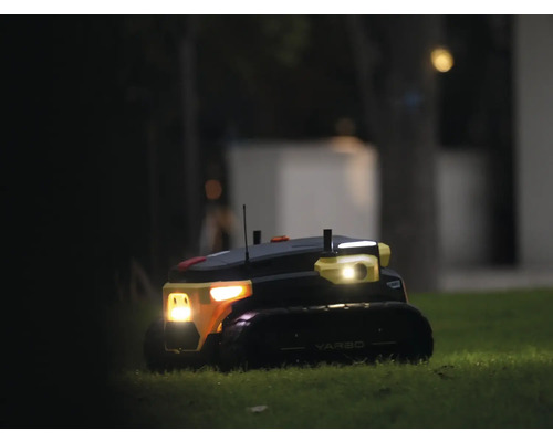 Robot de jardin autonome Yarbo sur une pelouse la nuit avec phares allumés.