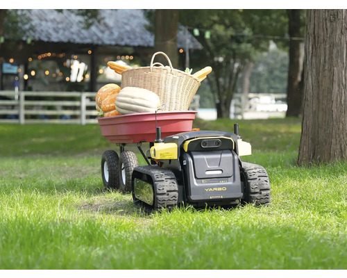 Un robot de jardin Yarbo à chenilles tractant une remorque de jardin rouge remplie de citrouilles et d'un panier en osier sur une pelouse.