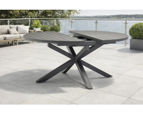 Table de jardin ronde extensible avec piètement en X et plateau à lattes sur une terrasse.