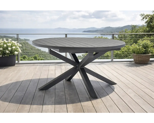 Table de jardin ronde moderne en métal avec un piètement en étoile sur une terrasse claire avec vue sur la mer.